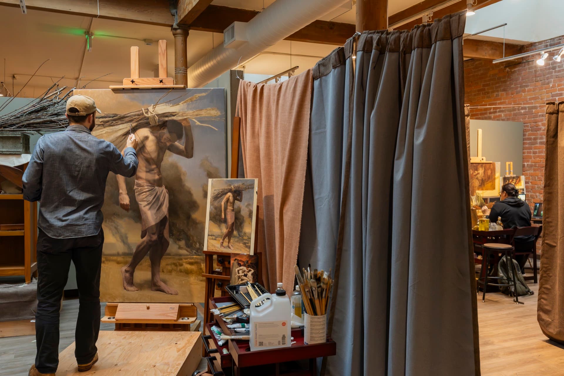 A painter working on a large figure painting beside the curtained studio bays upstairs at the Occidental