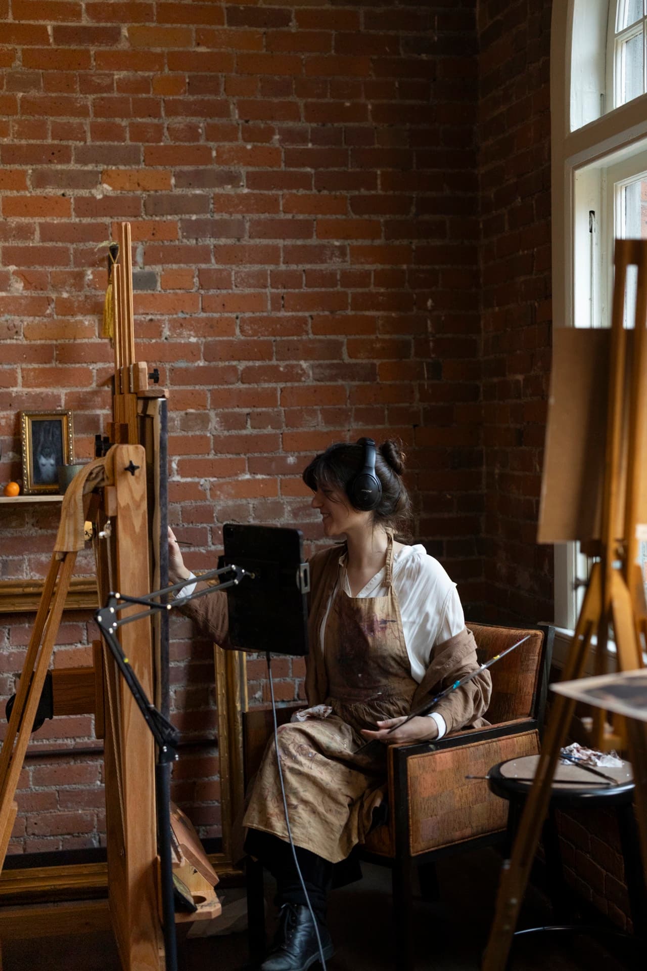 An artist painting at an easel in a brick-walled studio